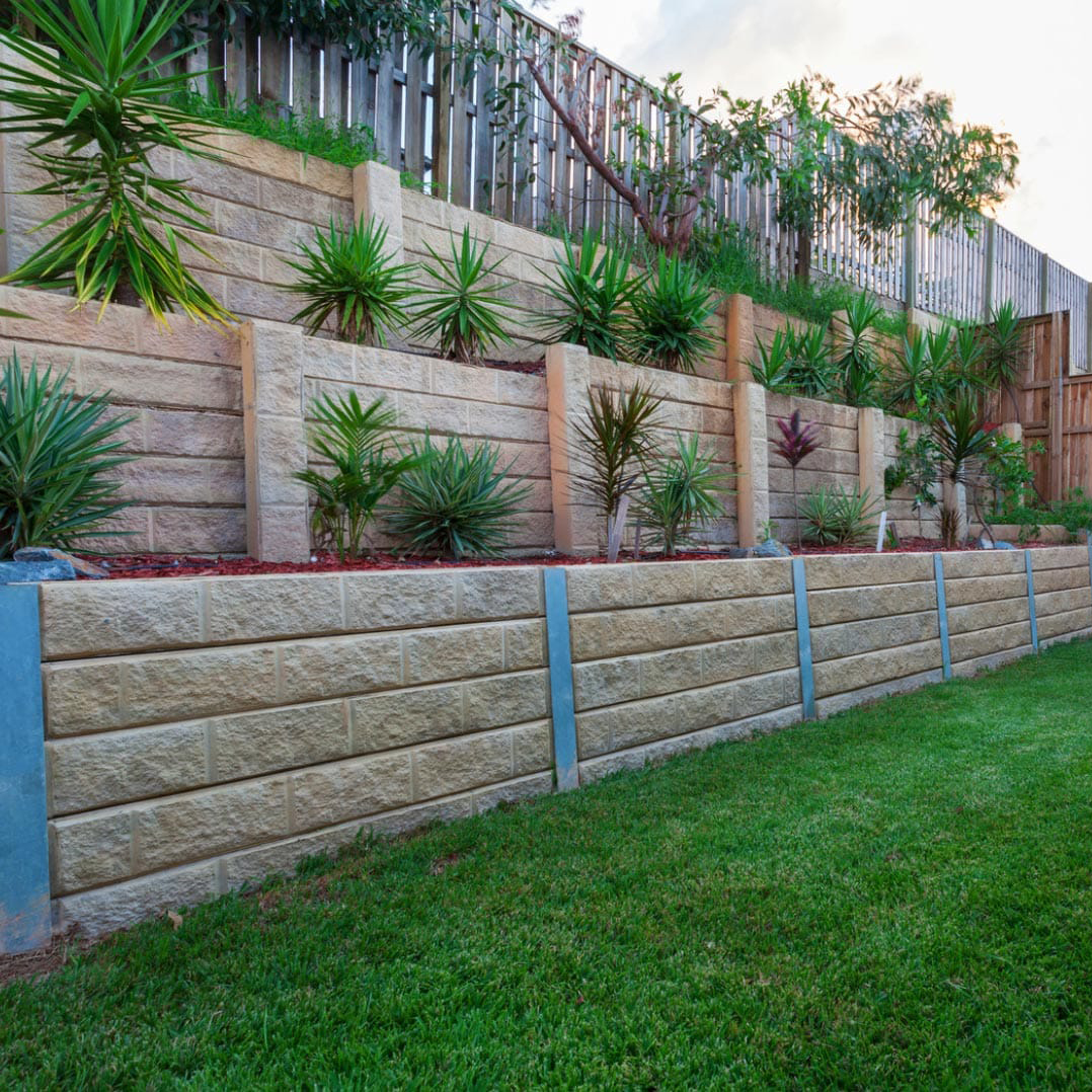 Tiered retaining walls with plants, shrubs, and green grass in a landscaped backyard.