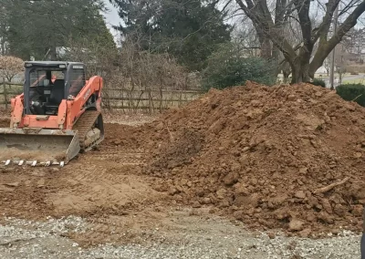 A bulldozer next to a large pile of dirt at a construction site with trees in the background.