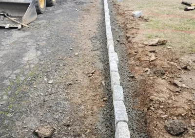 Granite curb stones being installed along the edge of a driveway with construction equipment nearby.