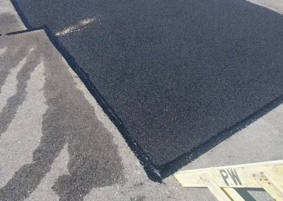 Freshly paved asphalt patch on a street, with workers and caution tape nearby.