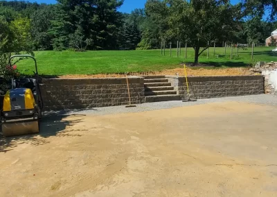 Freshly leveled dirt yard with stone steps, green lawn, trees, and construction equipment on the left.