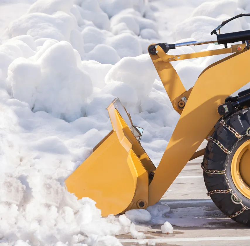 A yellow front loader with tire chains clears snow from a paved surface.